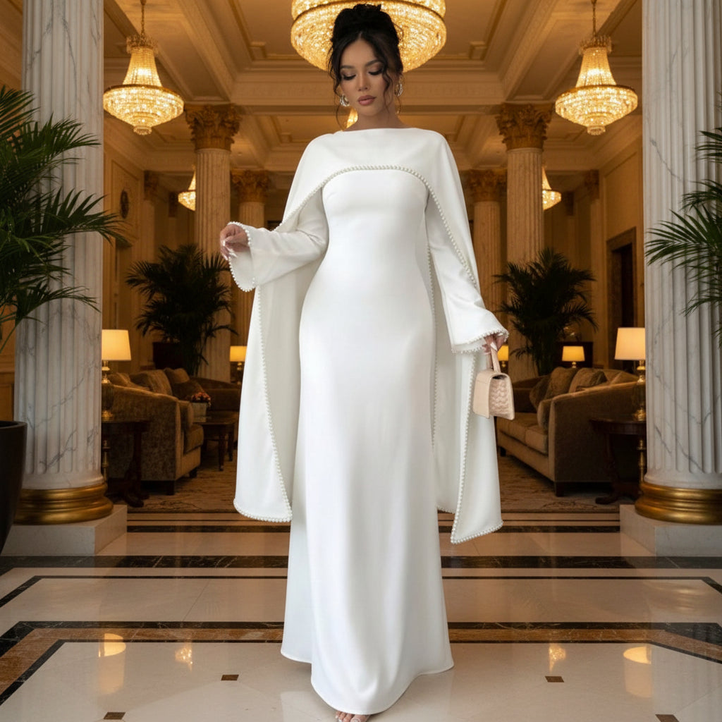 Woman wearing a long white dress with bell sleeves in a minimalistic setting.
