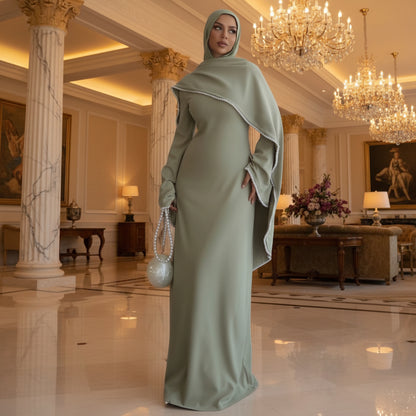 Woman in a long green dress standing in a room with a lamp and table in the background.