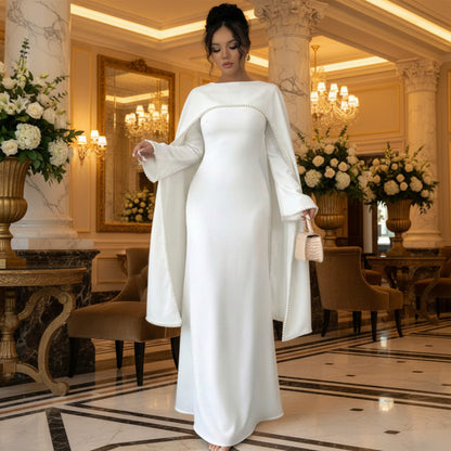 Woman wearing a long white dress with bell sleeves in a minimalistic setting.