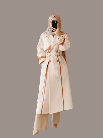 Anab Abaya elegant cream belted coat with brown contrast trim, lapel collar, and tailored fit worn by a woman.