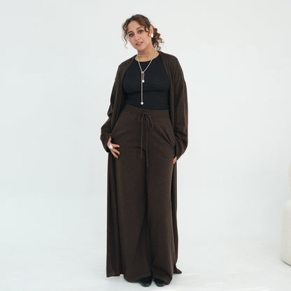 A woman modeling a dark brown two-piece outfit consisting of a long-sleeve cardigan and matching wide-leg drawstring pants, worn over a black top, against a plain white studio background.